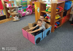 Dzieci siedzą w samochodzie zrobionym z pudełka